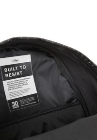 Svart Eastpak-väskas insida med en slät textur. Har en etikett med texten "Byggd för att motstå" och skötselråd.