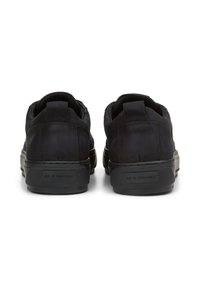 Un paio di sneakers nere low-top viste da dietro, con suole spesse e linguette sul colletto del tallone.