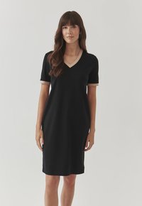 Black short-sleeve dress with a V-neck, featuring beige accents at the neck and sleeve hems, made from a smooth-textured fabric.