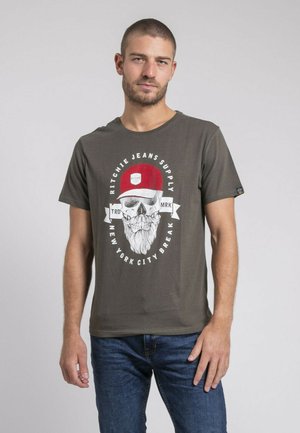 T-shirt en coton olive avec un graphique de skull blanc portant une casquette rouge et une barbe, avec le texte "Ritchie Jeans Supply" et un design vintage.