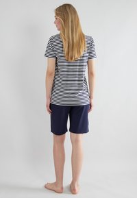 Camiseta de rayas en azul marino y blanco, combinada con pantalones cortos azul marino. La camiseta tiene mangas cortas y un dobladillo redondeado, con un corte clásico.