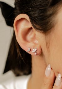 Silberne Ohrringe in Form von Schmetterlingen mit klaren, facettierten Edelsteinen, die aus zwei kleinen und einem größeren Akzentstein bestehen. Glatte Oberfläche, zartes Design.