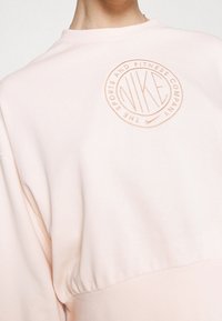 Světle růžová mikina s kulatým, vyraženým logem Nike ve tmavším odstínu. Měkká tkanina, volný střih, široké rukávy a žebrovaný lem.