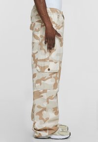 Beige kamuflasje cargo bukser med en avslappet passform, flere lommer, elastisk midjebånd og sydd detaljer, kombinert med lette sneakers.