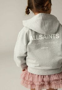 Sivá mikina s kapucňou a nápisom "ALLSAINTS TOKYO UNDERGROUND LONDON" na chrbte, skombinovaná s ružovou volánkovou tylovou sukňou.