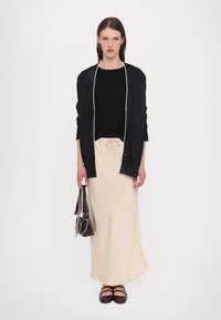 Black long-sleeve cardigan with a white trim over a black top, paired with a cream skirt and dark shoes. Accessories include a brown bag.
