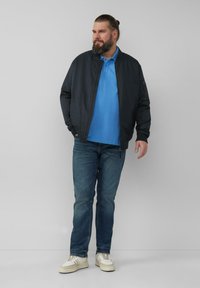 Donker bomberjack over een lichtblauwe polo, gecombineerd met een blauwe jeans en witte sneakers. Heeft een soepele textuur en een casual ontwerp.