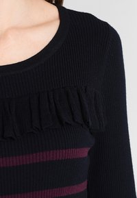 Navy ribbed top with a round neckline, featuring a ruffled accent along the chest and horizontal maroon stripes.