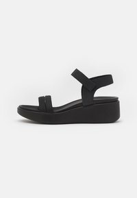 Sandalias de cuña negras con dos tiras anchas y una correa ajustable en el tobillo, hechas de un material suave con una suela texturizada.