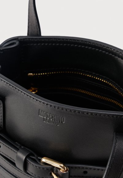 Sac à main Moschino en cuir noir avec boucle dorée et poche intérieure zippée visible, mettant en valeur le logo embossé à l'intérieur du sac.