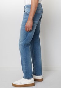 Lyseblå denimjeans med rett snitt, med klassisk fem-lomme-design og subtil falming. Brukt med hvite sneakers.