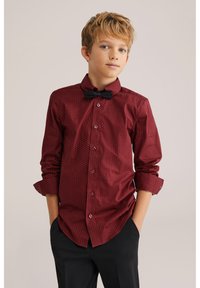 Rood gestreept shirt met lange mouwen en opgerolde manchetten, voorzien van kleine witte stippen en een zwarte vlinderdas, gecombineerd met zwarte broek.