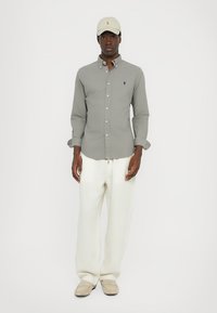 Sivina srajca s kratkimi rokavi, krema široke hlače, krema kapa in svetli natikači. Srajca ima logo in zavihane rokave.