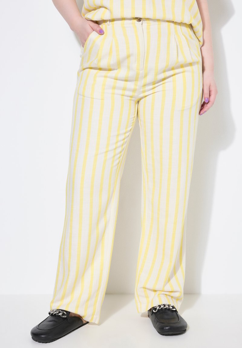 Geel en wit gestreepte wijde broek met zijzakken, zachte stof, geplooide voorkant en een ontspannen pasvorm, gecombineerd met zwarte schoenen.
