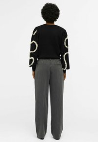 Pull noir avec des éléments décoratifs blancs le long des manches, associé à un pantalon gris taille haute, présentant une texture lisse et une coupe droite.