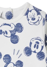 White fabric t-shirt featuring a blue cartoon pattern of Mickey Mouse faces and round ears, with a snap closure at the rounded neckline.