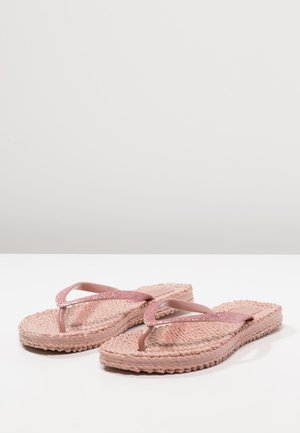 Lyserøde vævede flip-flops med glitrende lyserøde stropper, der hviler på en hvid overflade med en ensfarvet lys grå baggrund.
