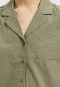 Olivově zelená košile na knoflíčky s límečkem, se širokým kapsou na prsou, měkkou texturou a lehkým materiálem.