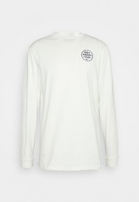 Long-sleeve, off-white cotton t-shirt with round neckline. Features circular navy logo, "Nike Athletic Club," on the left chest. Smooth texture.