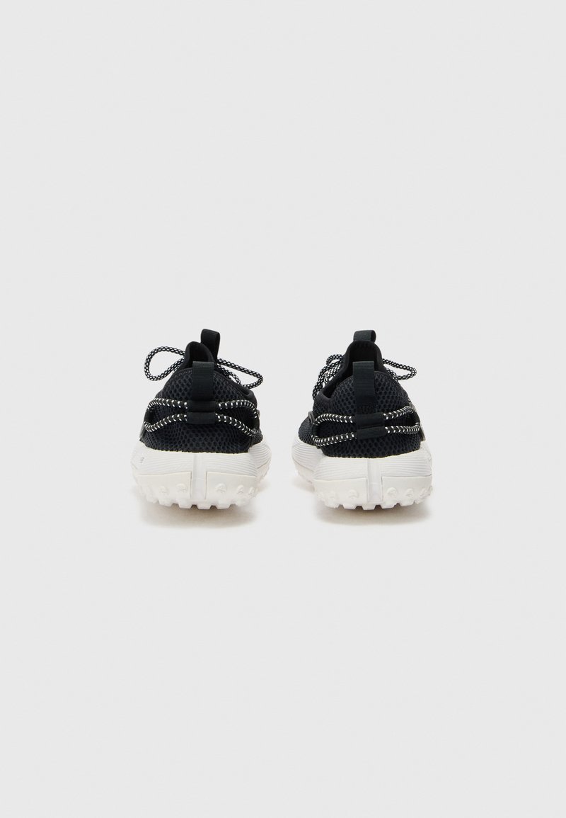 Zapatillas deportivas de malla negra con suelas de goma blanca, con detalles texturizados y cordones reflectantes, mostradas desde la parte posterior.