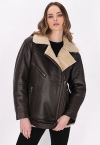 Giubbotto in pelle marrone con colletto in shearling beige, chiusura a zip asimmetrica e cinturino regolabile in vita. Finitura morbida e strutturata.