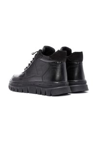 Zapatillas altas de cuero negro con acentos de ante, punta redonda, suela de goma gruesa que presenta un dibujo texturizado y letras en relieve alrededor de la base.