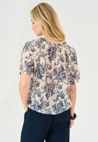 Bluse mit floralem Muster aus leichtem Stoff in Marineblau und Beige, mit gerafftem Ausschnitt und kurzen Ärmeln.