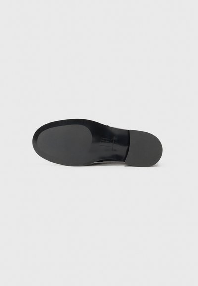 Suola delle scarpe in gomma nera con superficie liscia e design della punta arrotondata, senza marchi o dettagli di texture visibili.