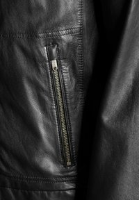 Schwarze Lederjacke mit sichtbarem Reißverschlussfach, eleganter Textur und maßgeschneiderter Naht entlang der Nähte. Weicher, matter Finish.