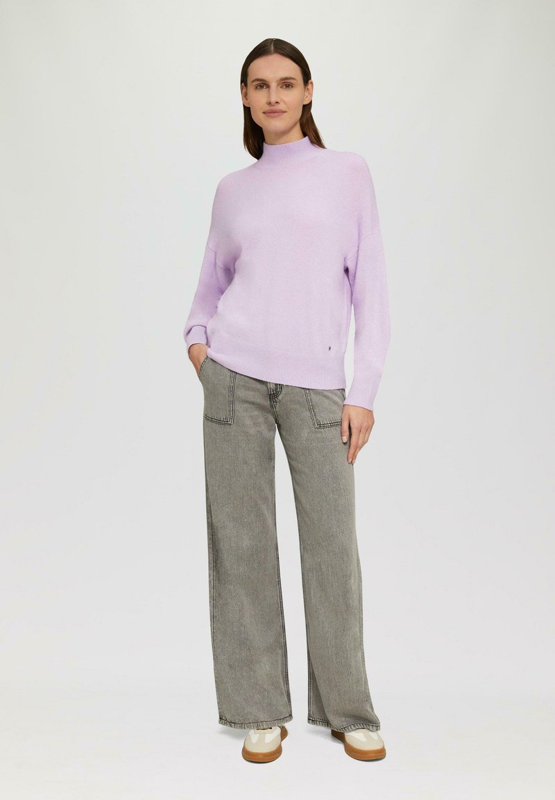 Hellblauer Strickpullover mit hohem Stehkragen, kombiniert mit grauen weit geschnittenen Jeans und cremefarbigen Sneakers. Sanfte Textur, lockere Passform.