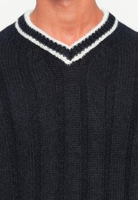 Sweater en maille navy avec des côtes verticales, doté d'un décolleté en V souligné par un col rayé blanc et noir. La texture semble épaisse.