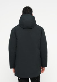 Čierna zateplená parka s vypchávkovaným designom, veľkou kapucňou, dlhými rukávmi a strednou dĺžkou. Hladká textúra bez viditeľného kovania alebo vzorov.