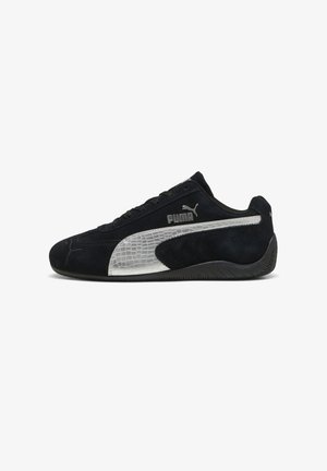 Musta Puma-tossu hopeisella teksturoidulla raidalla ja logolla, mokkanahkainen päälliosa, nauhallinen malli ja musta kumipohja, sivuprofiili.