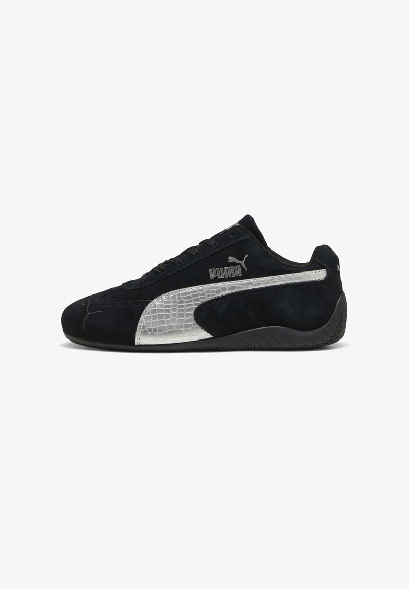 Mustad Puma tossud hõbedase tekstuuriga triibu ja logoga, seemisnahast pealsega, paeltega kinnituv disain ja musta kummist tald, külgvaade.