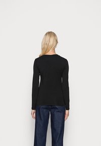 Černý dlouhý rukáv top vyrobený z měkké tkaniny s kulatým výstřihem, přiléhavým střihem a hladkým povrchem, spárovaný s tmavými džínovými kalhotami.