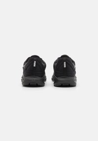 Las zapatillas deportivas negras cuentan con una parte superior texturizada con detalles de malla, un diseño de talón redondeado y un acento de logo en la parte trasera.