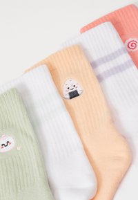 Fem par farverige sokker: lysegrøn, hvid med striber, fersken med et risbolddesign og lyserød med swirl-detalje. Blød, ribbet tekstur.