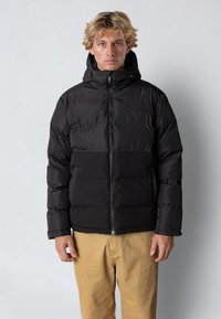 Svart puffjacka med dragkedja framtill och huva. Har quiltad textur, justerbara snoddar och en enfärgad design utan mönster.