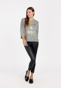 Maglietta oversize grigia con la scritta dorata "ROCK & ROLL", abbinata a leggings in pelle nera e scarpe basse nere. Design dell'outfit semplice e casual.