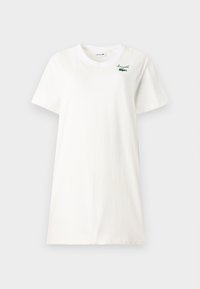 Valkoinen puuvillapaita, jossa on pyöreä kaula-aukko, lyhyet hihat ja vihreä Lacoste-logo brodeerattuna vasemmassa rinnassa.
