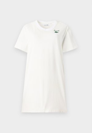Valge puuvillane T-särk, millel on ümmargune kaelus, lühikesed varrukad ja rohelise Lacoste'i logo, mis on tikitud vasakule rinda.