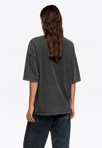 Sivá voľná tričko s krátkymi rukávmi a uvoľneným strihom, s poškodenou textúrou. Skombinované s tmavomodrými džínsami.