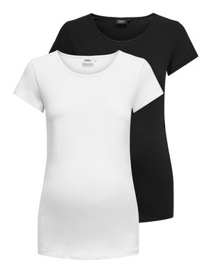 Mujer embarazada de pie, con una camiseta blanca ajustada de manga corta, pantalones negros y zapatillas blancas, sobre un fondo claro y liso.