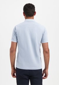 Lichtblauwe polo met een subtiele textuur, korte mouwen en een traditionele kraag. Geen zichtbare patronen of hardwaredetails.