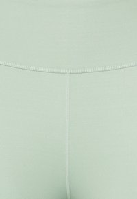 Leggings a vita alta di un delicato verde menta, realizzati in un tessuto liscio con un leggero lucido, dotati di cuciture piatte e senza motivi visibili.