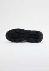 Semelle de chaussure en caoutchouc noir avec un motif de semelle décoré de rainures profondes et de crampons multi-directionnels pour une traction et une stabilité optimales.