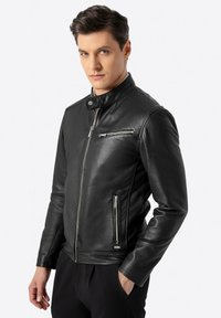 Schwarze Lederjacke mit hohem Kragen, Frontreißverschluss und Reißverschlusstasche auf der Brust. Hat ein tailliertes Design und eine glatte Oberfläche.