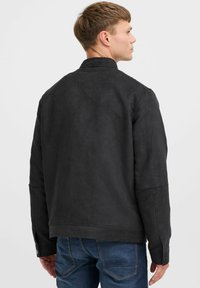 Zwarte faux suede jas met een opstaande kraag, lange mouwen en knoopsluitingen bij de mouwen. Soepele textuur, minimalistisch ontwerp en getailleerde pasvorm.