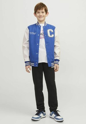 Blå varsityjacka med vita ärmar, "C"-loge, randiga muddar, vit t-shirt under, svarta byxor och blå sneakers med vita detaljer.