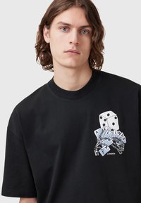 Black cotton t-shirt featuring a graphic of dice and playing cards with skeletal hands, round neckline, and short sleeves.